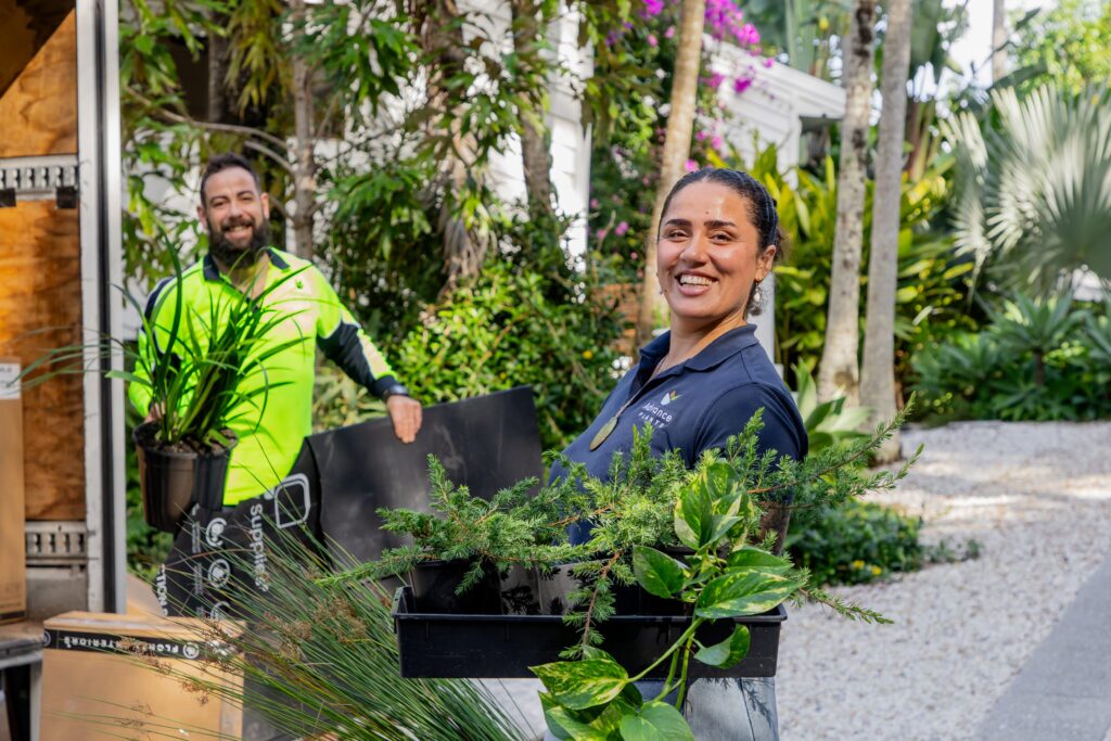 Two Advance Plants technicians unloading potted plants and greenery from a delivery truck at a lush garden site