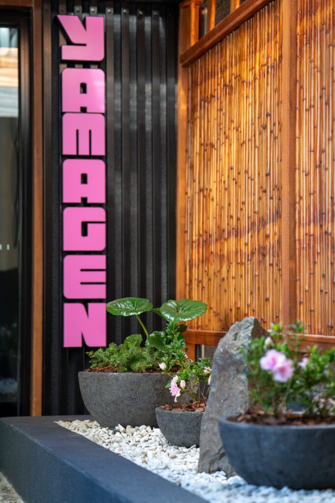 Tractor-seat plant and azalea in dark stone bowls beneath the neon Yamagen sign at QT Gold Coast